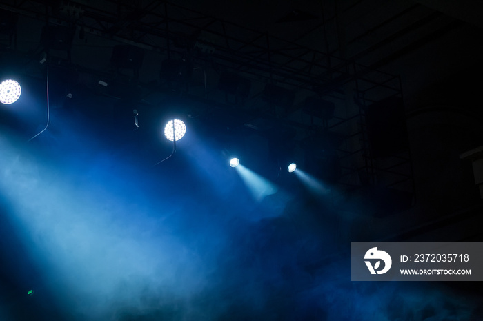 Rays of spotlights illuminate the concert stage with blue light against a dark background.