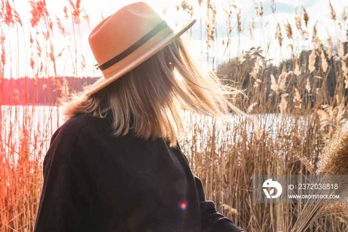 European blonde woman with beige hat in black sweater in the countryside. Golden hour, cottagecore. 