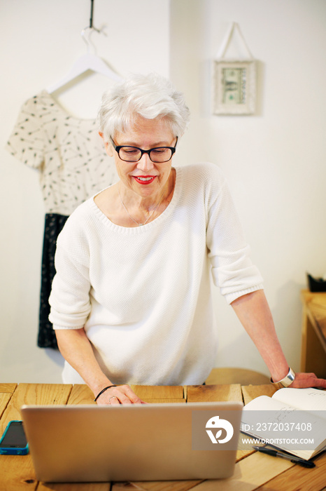 Senior woman working on laptop in clothing store