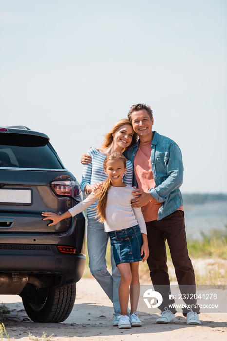 Selective focus of family looking at camera near car on beach