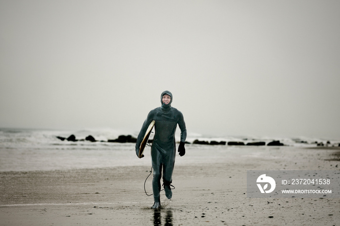 Portrait of man in wetsuit with surfboard running on beach