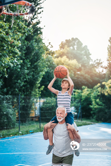 Grandfather and his grandson enjoying in beautiful sunny day and playing basketball.