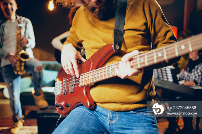 Close up of bass guitarist playing guitar while sitting on the chair. In background rest of the band