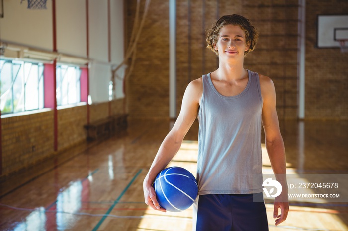 Portrait of smiling young man with basketball standing in court