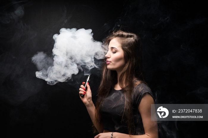 Attractive young woman vaping and blowing smoke isolated on black background