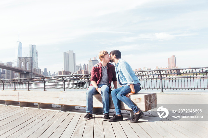 Male couple kissing on riverside by Brooklyn Bridge, New York, USA