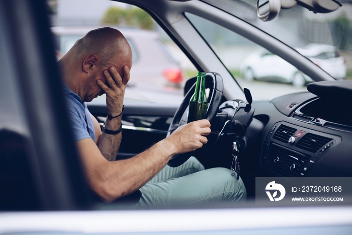 Drunk driver drinking alcohol in car and holding beer bottle