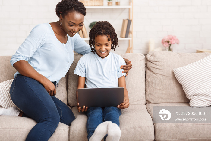非洲妈妈和女儿在沙发上使用笔记本电脑