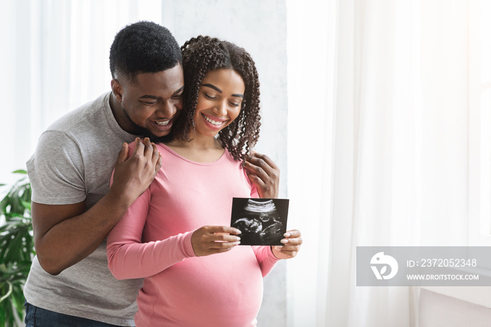 Smiling pregnant black couple showing ultrasound image of their baby