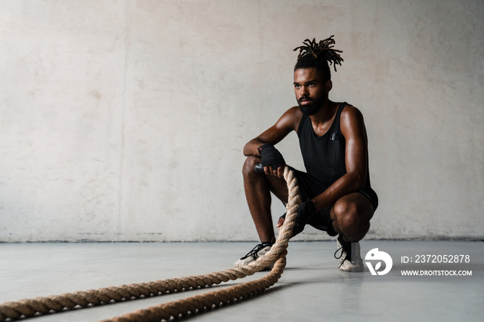 Image of african american sportsman working out with battle ropes