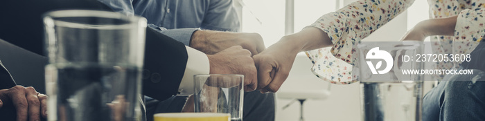 Wide view image of three business people bumping their fists together as they sit in an office meeti