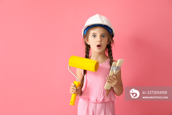 Surprised little girl with paint roller and brushes on pink background