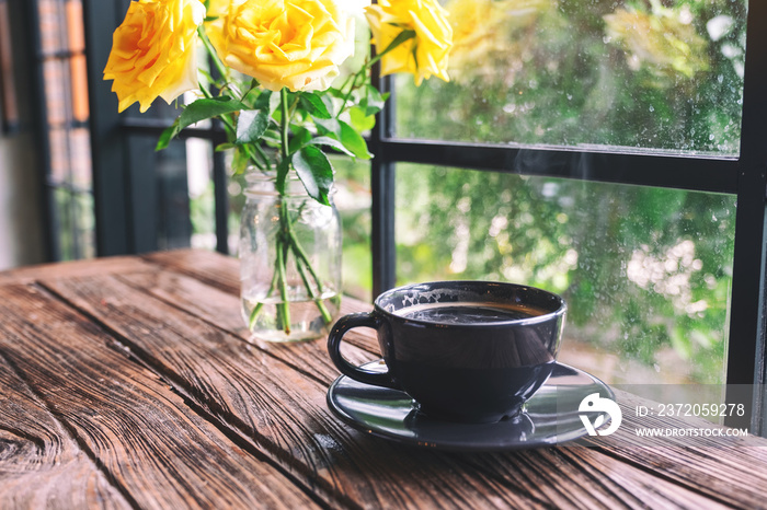 复古木桌上花瓶里一杯黑咖啡和黄玫瑰的特写图片