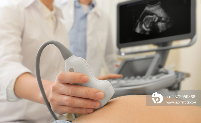 Doctor conducting ultrasound examination of pregnant woman in clinic, closeup