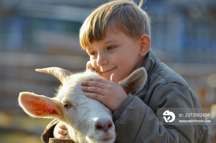 Joyful and happy boy hugs and strokes a horned goat, the concept of the unity of nature and man.