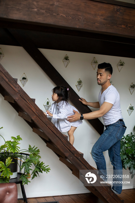 Side view of father assisting daughter in climbing wooden steps at home