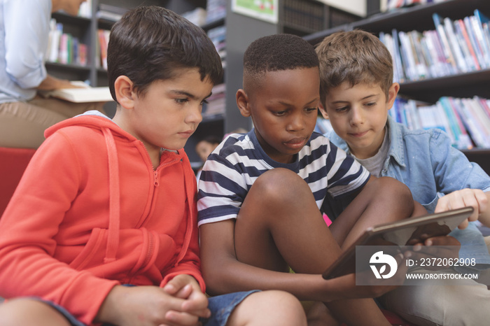 Schoolboys using a digital tablet while they are sitting on cushions in a library