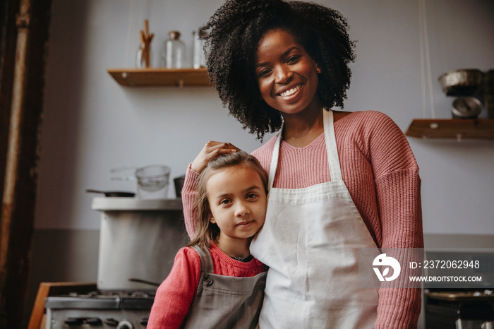 Portrait of smiling female chef with cute student standing against wall in cooking class