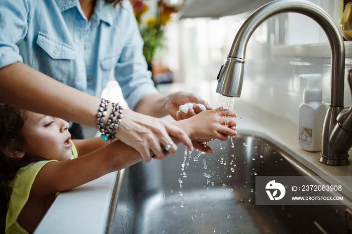 Mother and daughter washing hands in kitchen sink at home