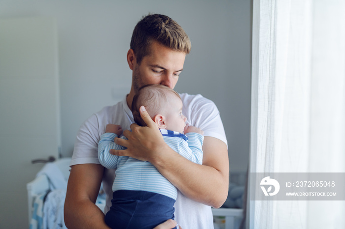 关爱白人的年轻父亲站着抱着他可爱的6个月大的儿子的画像