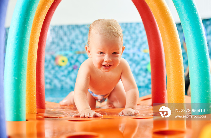 Very cute interesting little boy is crawling on a floating colorful construction in the swimming poo