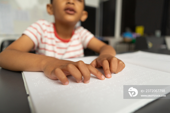 Blind schoolboy hands reading a braille book in classroom