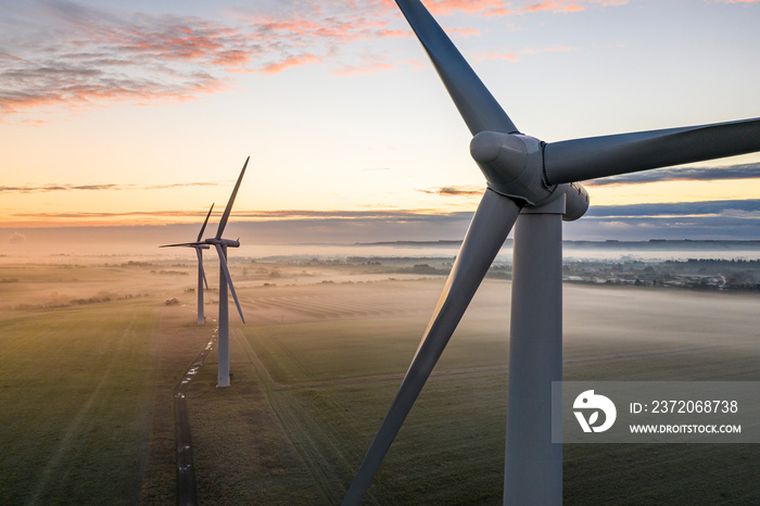 Aerial view of three wind turbines in the early morning fog at sunrise in the English countryside