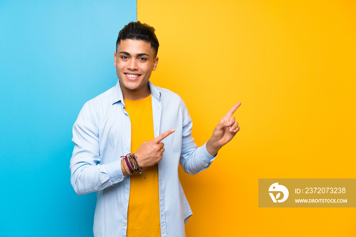 Young man over isolated colorful background pointing finger to the side