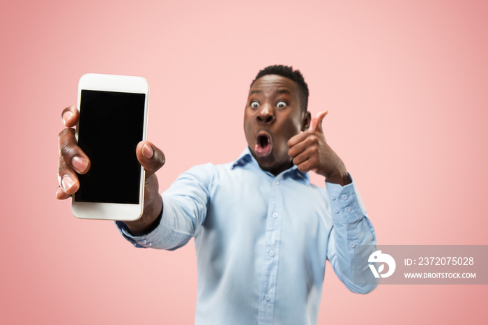 Indoor portrait of attractive young black african man isolated on pink background, holding blank sma