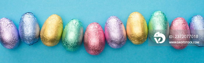 Top view of chocolate Easter eggs in colorful foil on blue background, panoramic shot