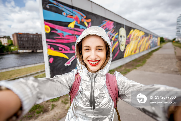 Young woman tourist making selfie photo standing in front of the Berlin wall in Germany