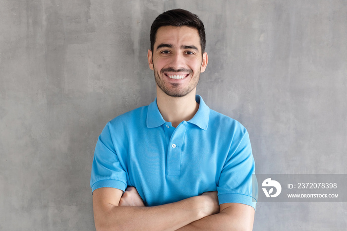 Smiling handsome man in blue polo shirt standing with crossed arms, standing against gray textured w