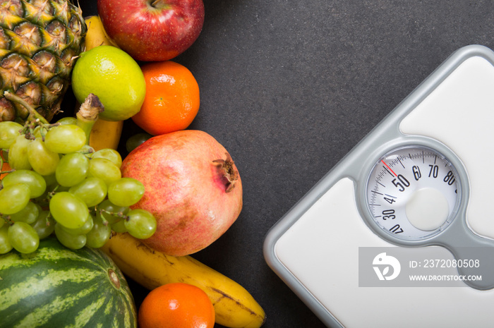 Stack of fruits and white weight scale on stone countertop.