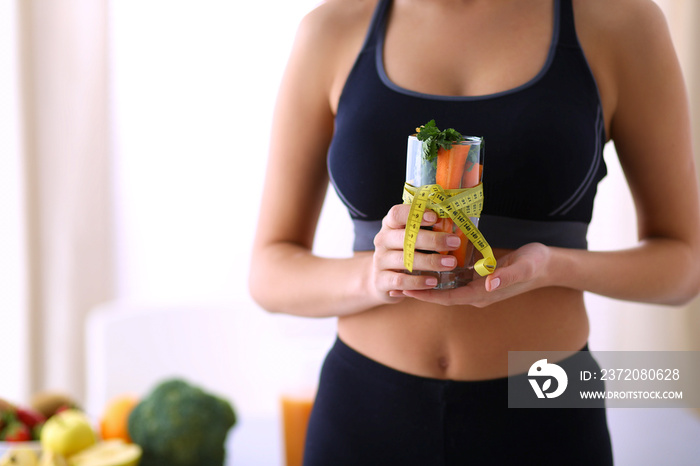 Woman holding a drinking glass full of fresh fruit salad with a tape measure around the glass