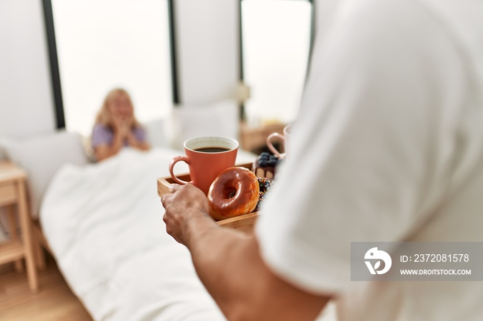 Man surprising his girlfriend with breakfast on the bed at home.