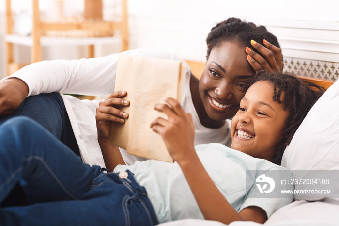 Happy black family reading book in bedroom