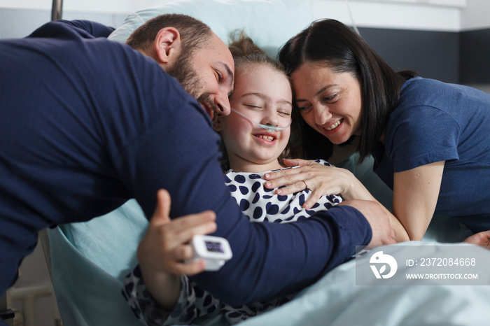 快乐的年轻父母在儿科诊所拥抱住院康复的小女儿