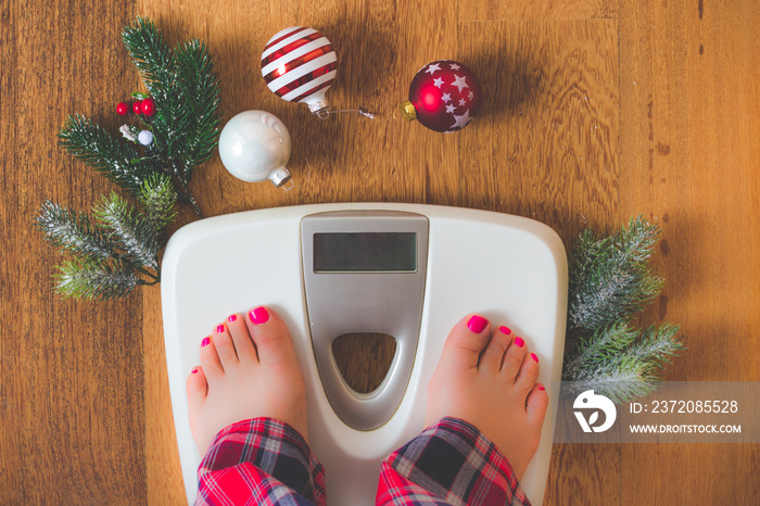 Top view of female feet in winter pajamas on digital scales or weight scale on wooden background sur