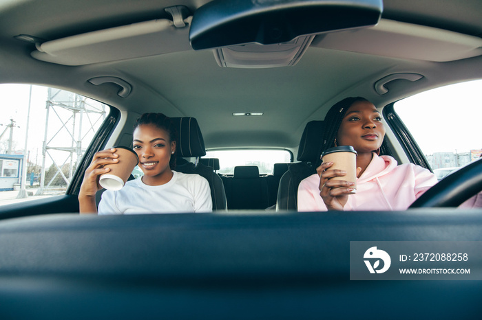 Young two african women sitting in car drinking coffee go on the way to road. African woman drinking