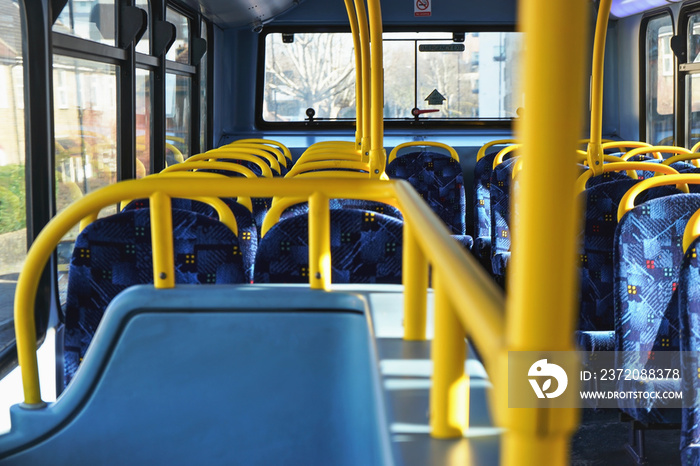 Sun shines on empty interior of London double decker bus, yellow holding rails and blue seats