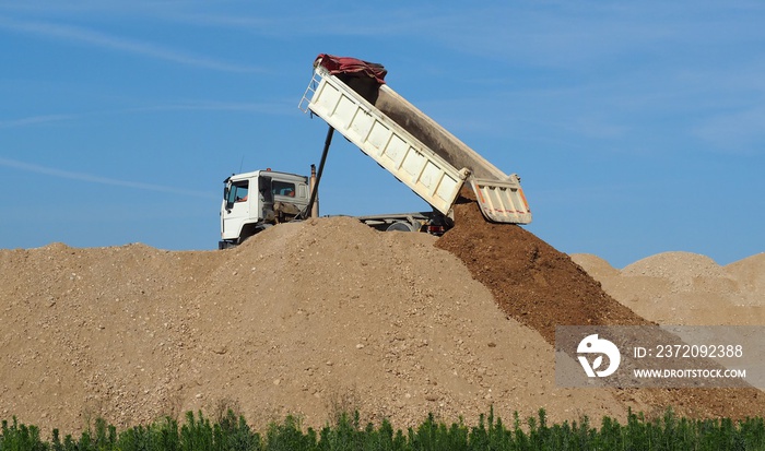 Dump truck unloading soil on the top of  dunes