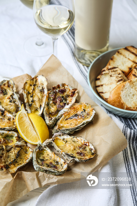 Tasty baked oysters with grilled bread and white wine on table