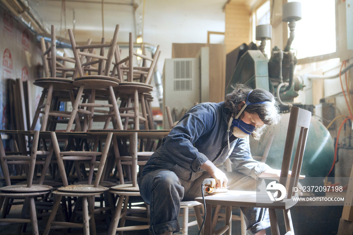 Female carpenter sanding wooden chair at workshop