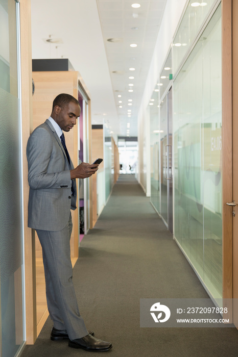 Businessman using smart phone in office corridor