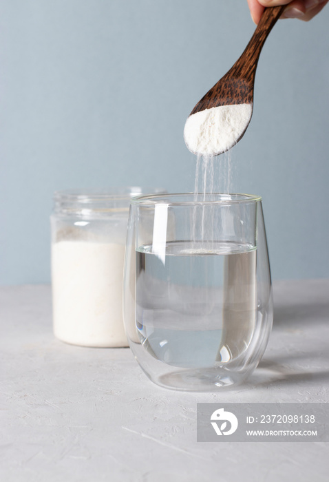 Collagen powder is add to glass of water with a spoon. Healthy and anti-age concept on light blue ba