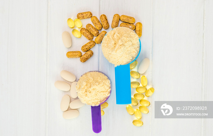 Closeup blue and purple measure dishes with protein powder and white-yellow sport pills around on th