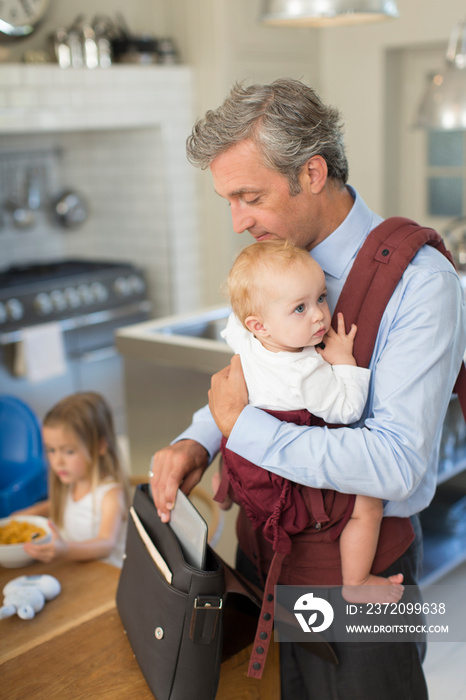 Businessman father preparing for work with baby son in carrier