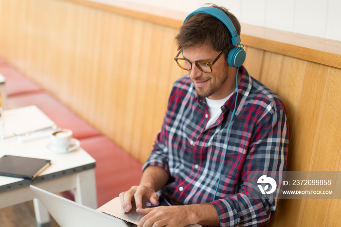 Smiling man with headphones working at laptop in cafe