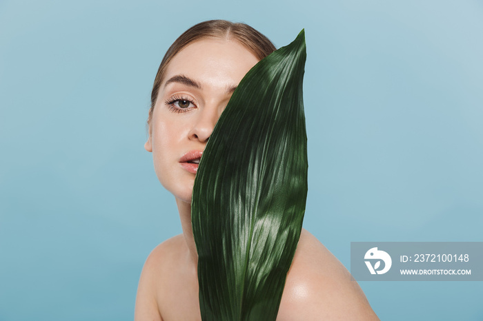 Beautiful young woman take care of her skin isolated over blue wall background posing with leaf flow