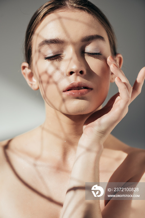 portrait of tender nude girl with closed eyes and shadows on face on grey